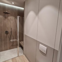 Meblowy Design Arkadiusz Grzywna - Nowoczesna łazienka z zabudową meblową w odcieniach szarości, kabina prysznicowa typu walk-in z deszczownicą, wisząca miska WC i podłoga imitująca drewno.