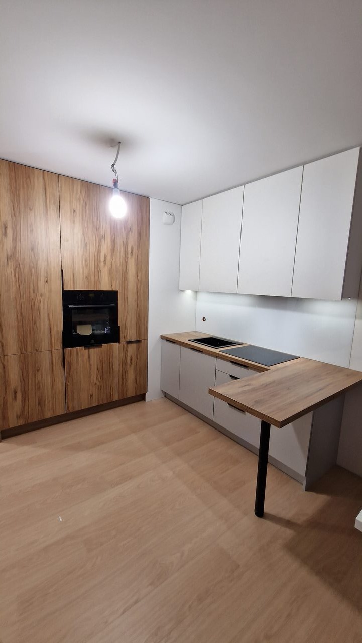 Nowoczesna kuchnia na wymiar z drewnianymi frontami szafek i wbudowanym piekarnikiem, połączona z białymi szafkami i blatem roboczym z wysuwanym blatem jadalnym na jednej nodze.