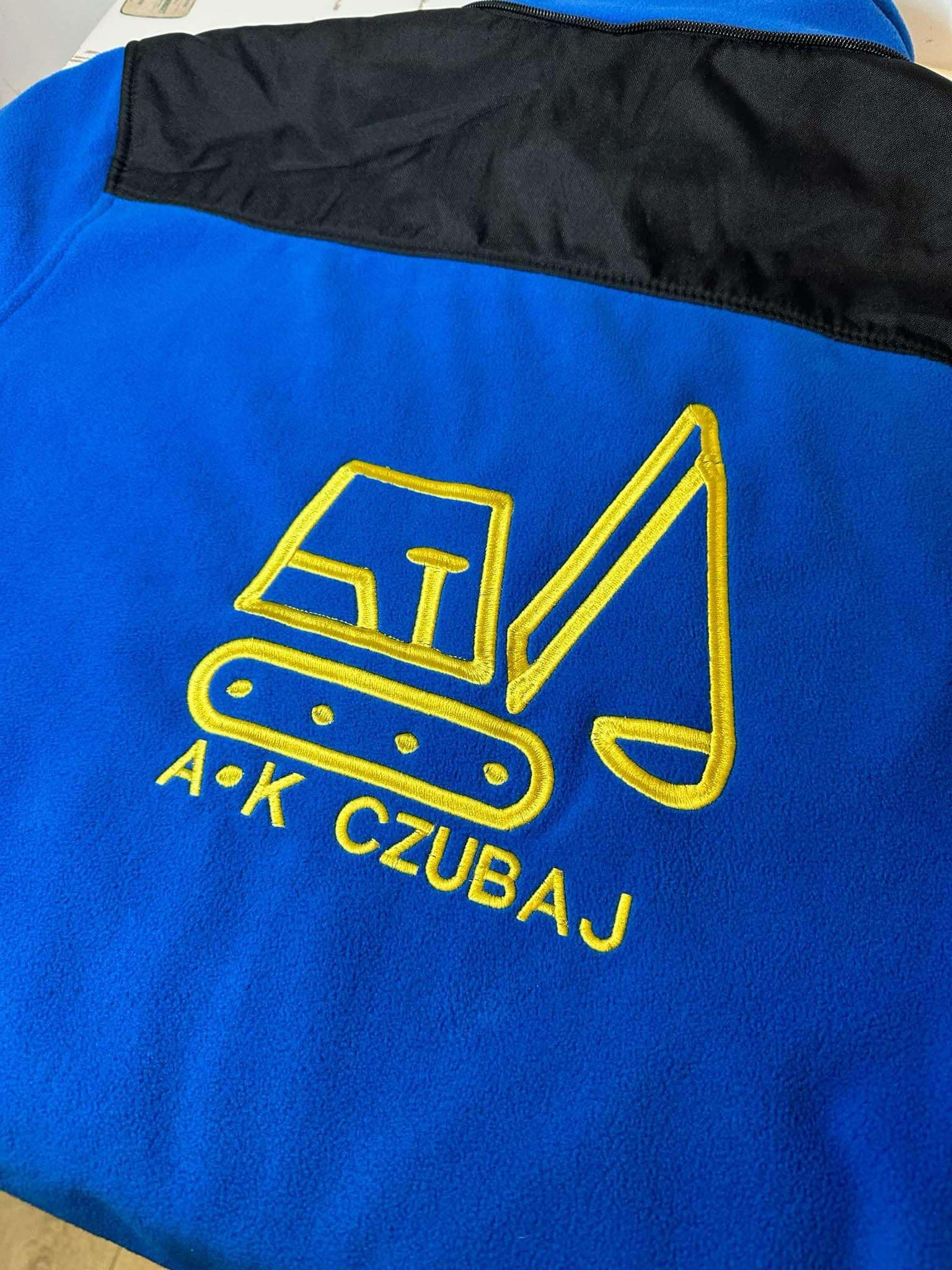 Niebieska bluza polarowa z czarnym karczkiem i wyhaftowanym żółtym logo koparki oraz napisem 'A.K CZUBAJ' wykonanym haftem w Tarnowskich Górach.