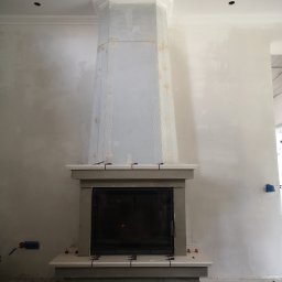 VOLHA PAVIADAIKA - Wnętrze w Gdańsku w trakcie prac wykończeniowych, widoczny kominek z obudową w surowym stanie, ściany po nałożeniu gładzi, widoczne narzędzia i materiały budowlane.