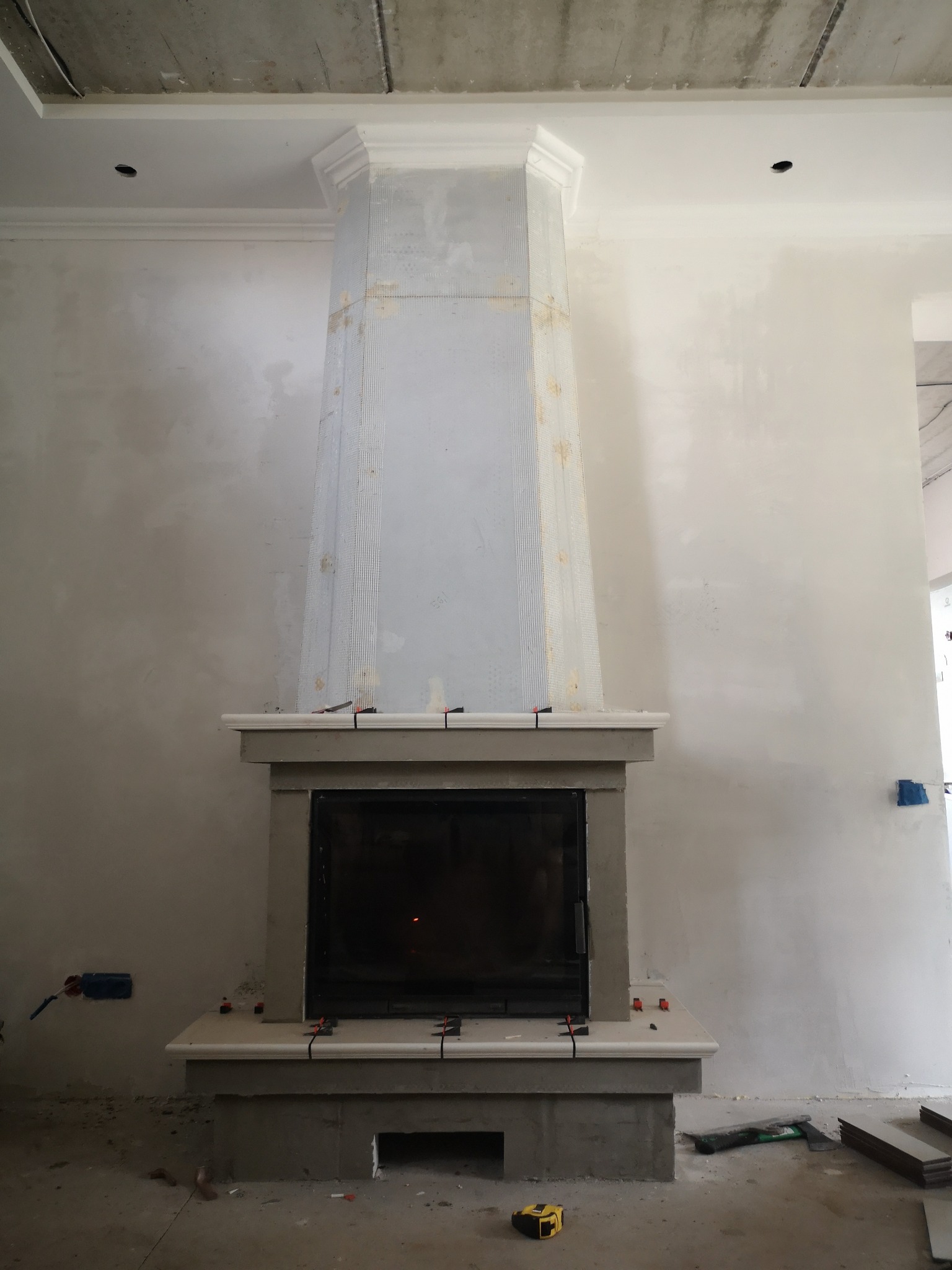 Wnętrze w Gdańsku w trakcie prac wykończeniowych, widoczny kominek z obudową w surowym stanie, ściany po nałożeniu gładzi, widoczne narzędzia i materiały budowlane.