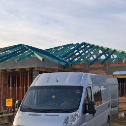 Tab-Dach - Srebrny furgon Citroen na tle budowy domu z widoczną konstrukcją dachu z impregnowanego na niebiesko drewna i fragmentem murowanych ścian.