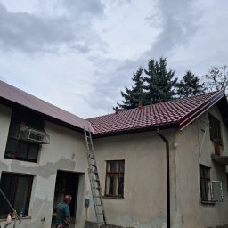 Tab-Dach - Dom z nowym, czerwonym dachem z blachodachówki, widoczna drabina oparta o ścianę i mężczyzna stojący przed budynkiem.