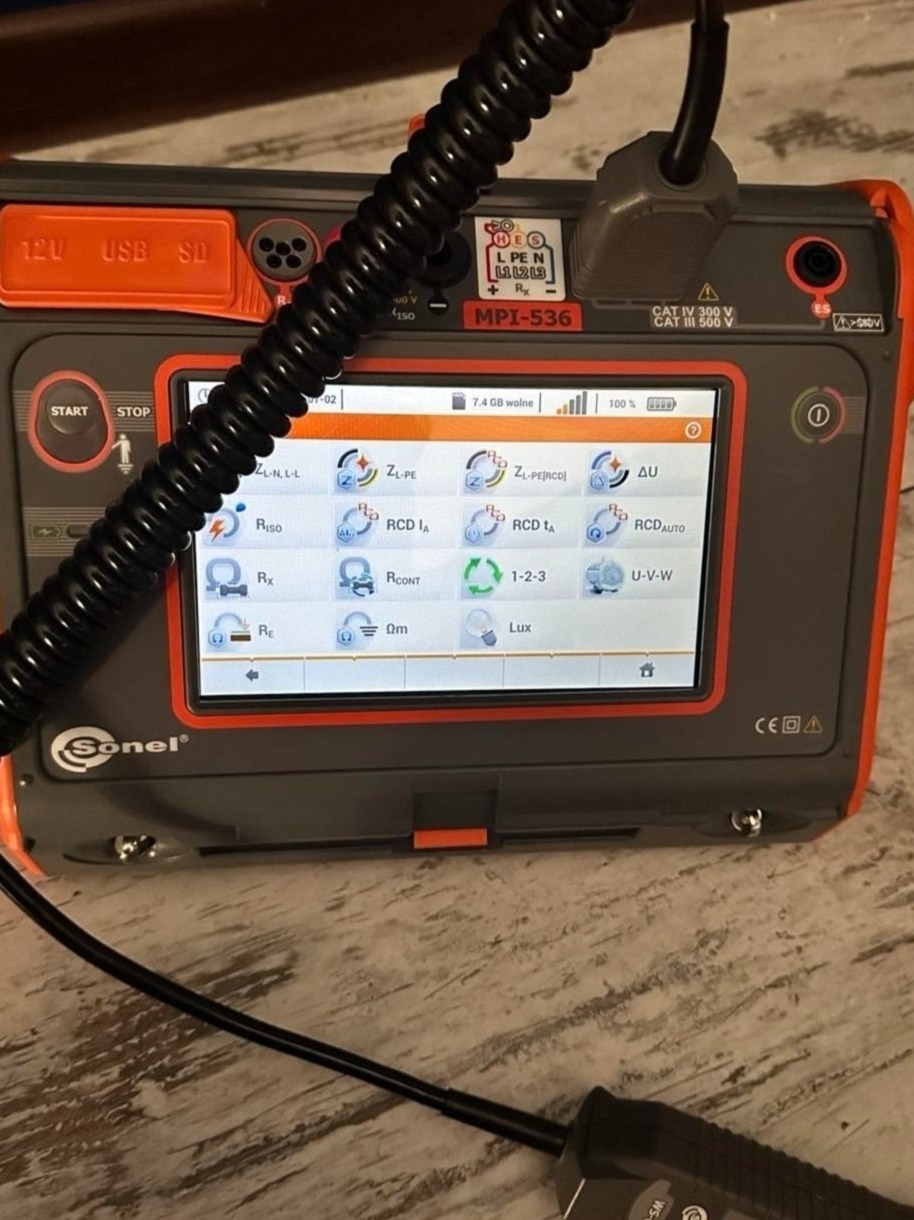 Miernik elektryczny Sonel MPI-536 z wyświetlaczem pokazującym różne opcje pomiarowe, kabel pomiarowy podłączony, widoczne gniazda USB i SD.