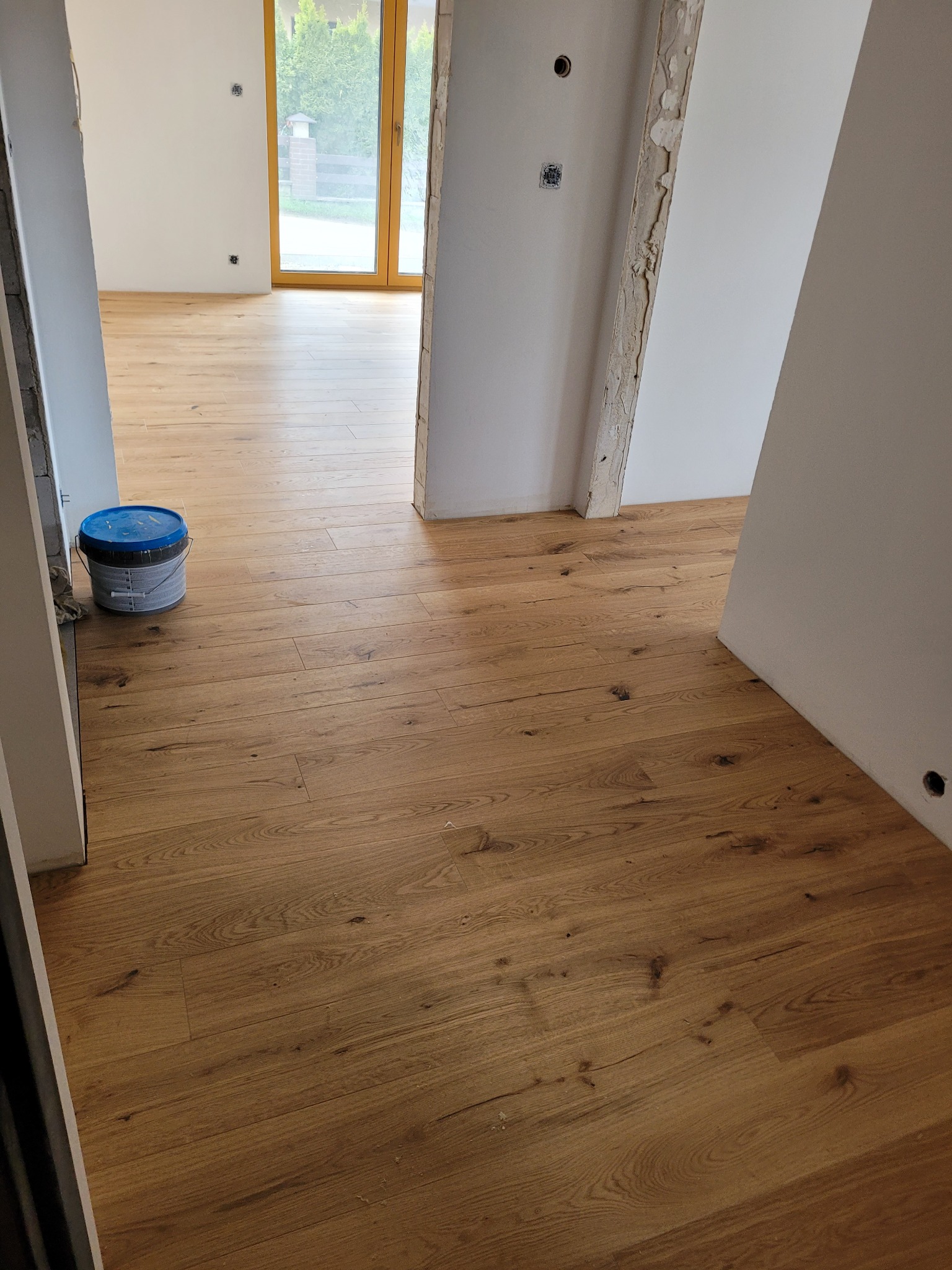 Jasny parkiet ułożony w nowym domu, widoczna puszka z farbą i fragmenty ścian w trakcie wykańczania.