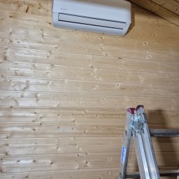 DM5 Daniel Mazuruk - Biała klimatyzacja Rotenso zamontowana na drewnianej ścianie poddasza, widoczna drabina Krause. Ujęcie z dołu, podkreślające instalację w trudnych warunkach.