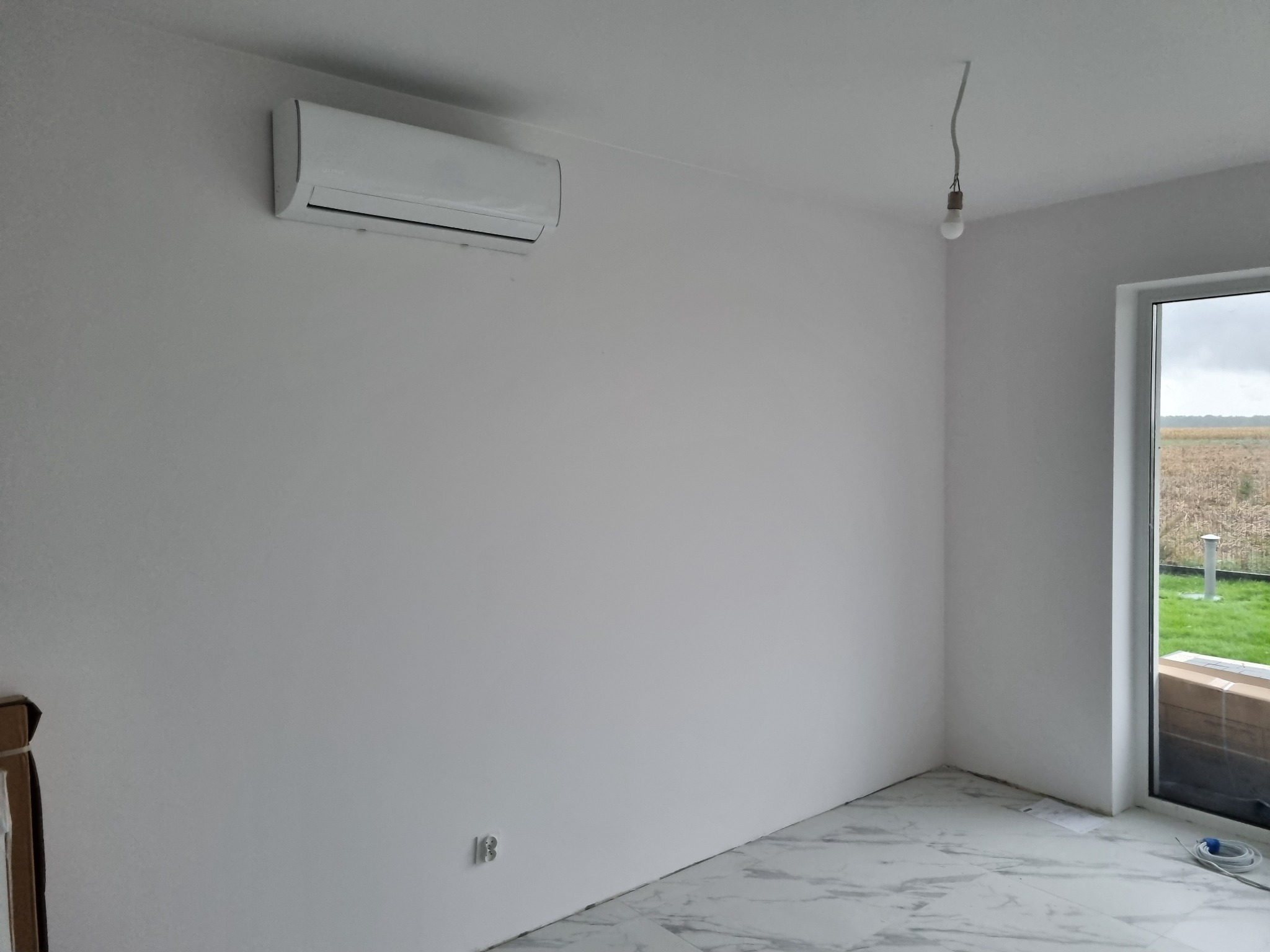 Nowoczesny, biały klimatyzator ścienny w jasnym pokoju z marmurową podłogą, widok na zewnątrz przez okno. Minimalistyczny design wnętrza.