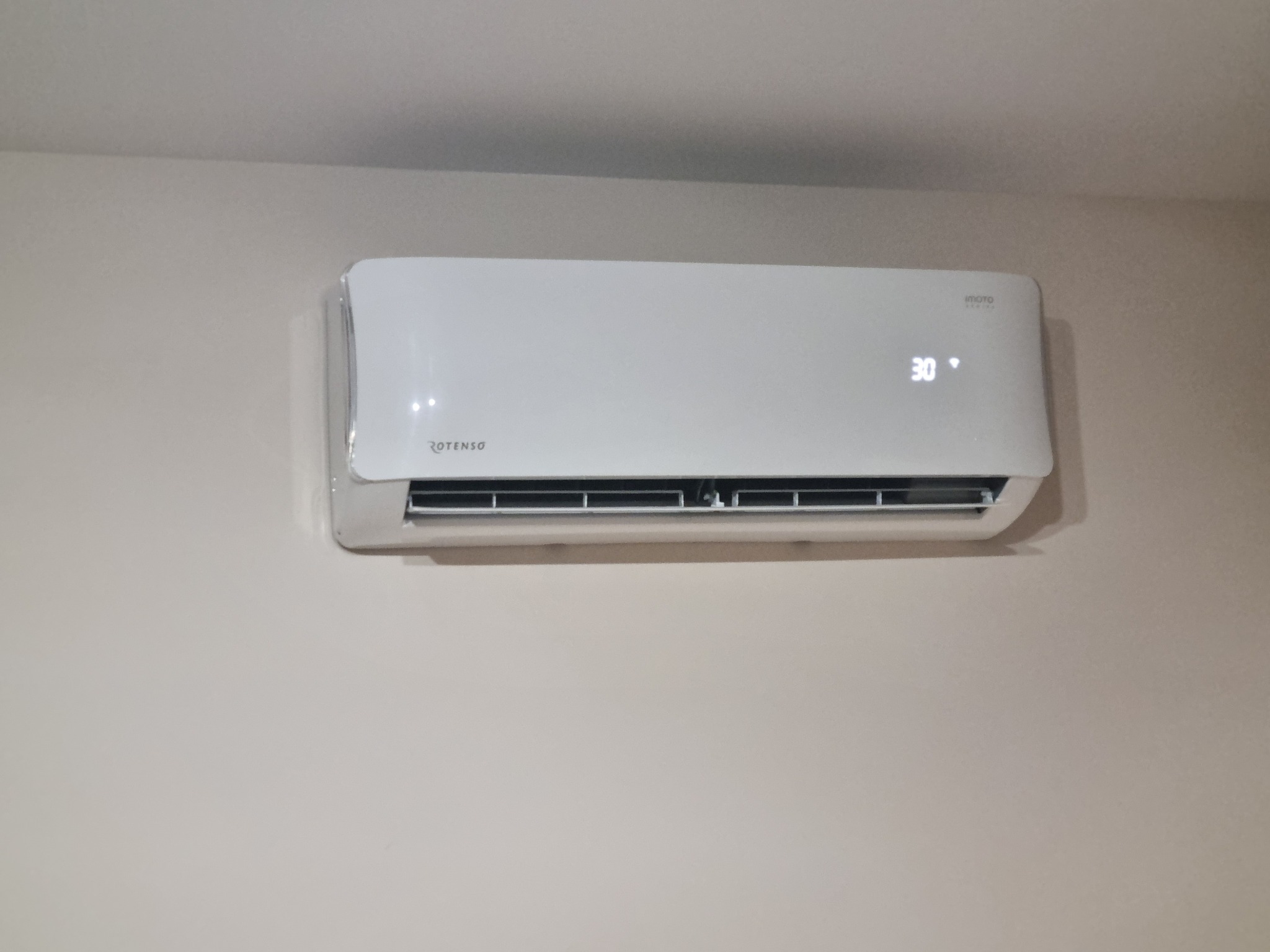 Biała klimatyzacja Rotenso z wyświetlaczem 30 stopni Celsjusza, zamontowana na jasnej ścianie. Widok centralny, bez dodatkowych elementów.