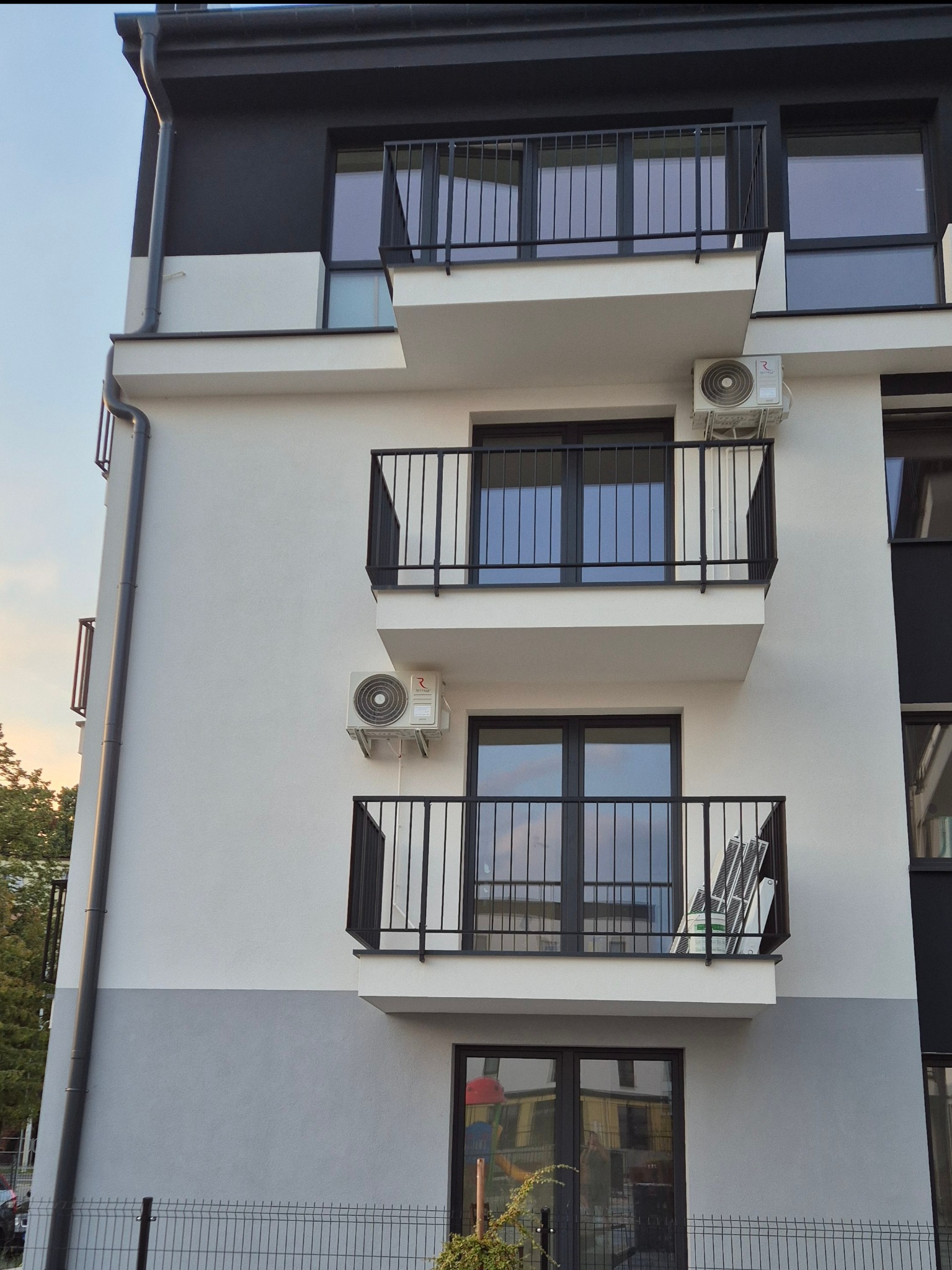 Elewacja budynku z balkonami i zainstalowanymi klimatyzatorami. Widoczne jednostki zewnętrzne klimatyzacji na białej fasadzie budynku.