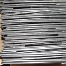 Stos strzemion zbrojarskich ułożonych równolegle w kartonowym pudełku, widoczne ślady rdzy na metalu.