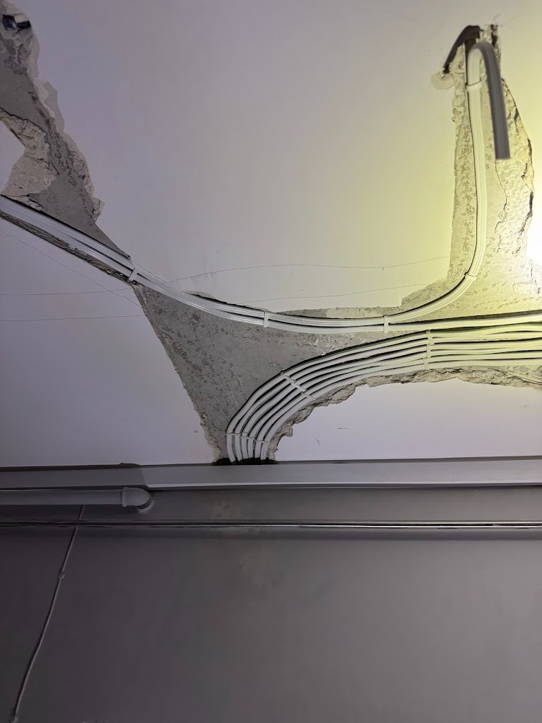 Wiązka białych kabli elektrycznych prowadzona w bruzdach w suficie, częściowo zamaskowanych gipsem, widoczne niedoskonałości i nierówności tynku.