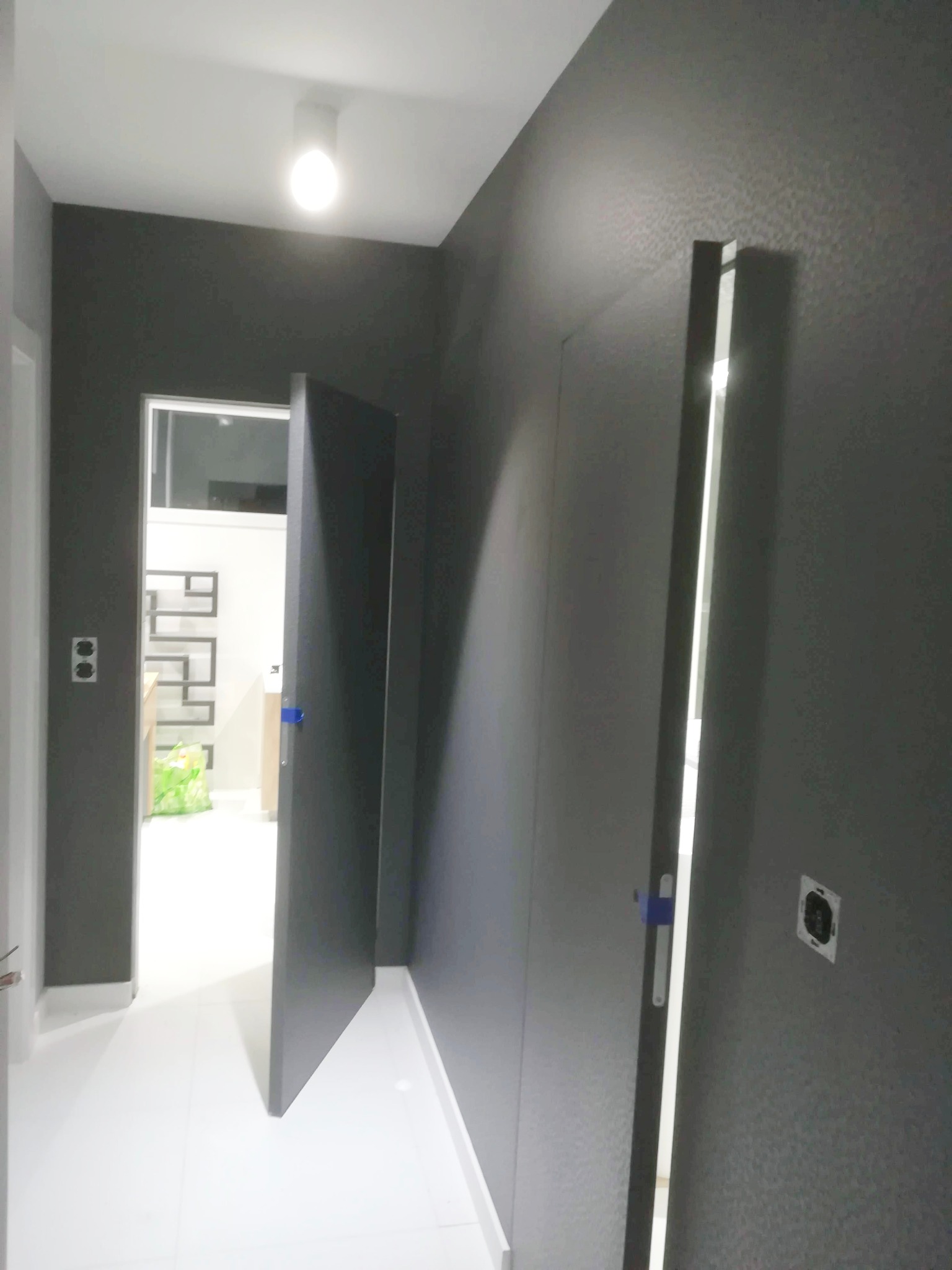 Pomieszczenie po malowaniu na szaro, widoczne dwie otwarte, szare drzwi, biała podłoga z płytek i białe listwy przypodłogowe.