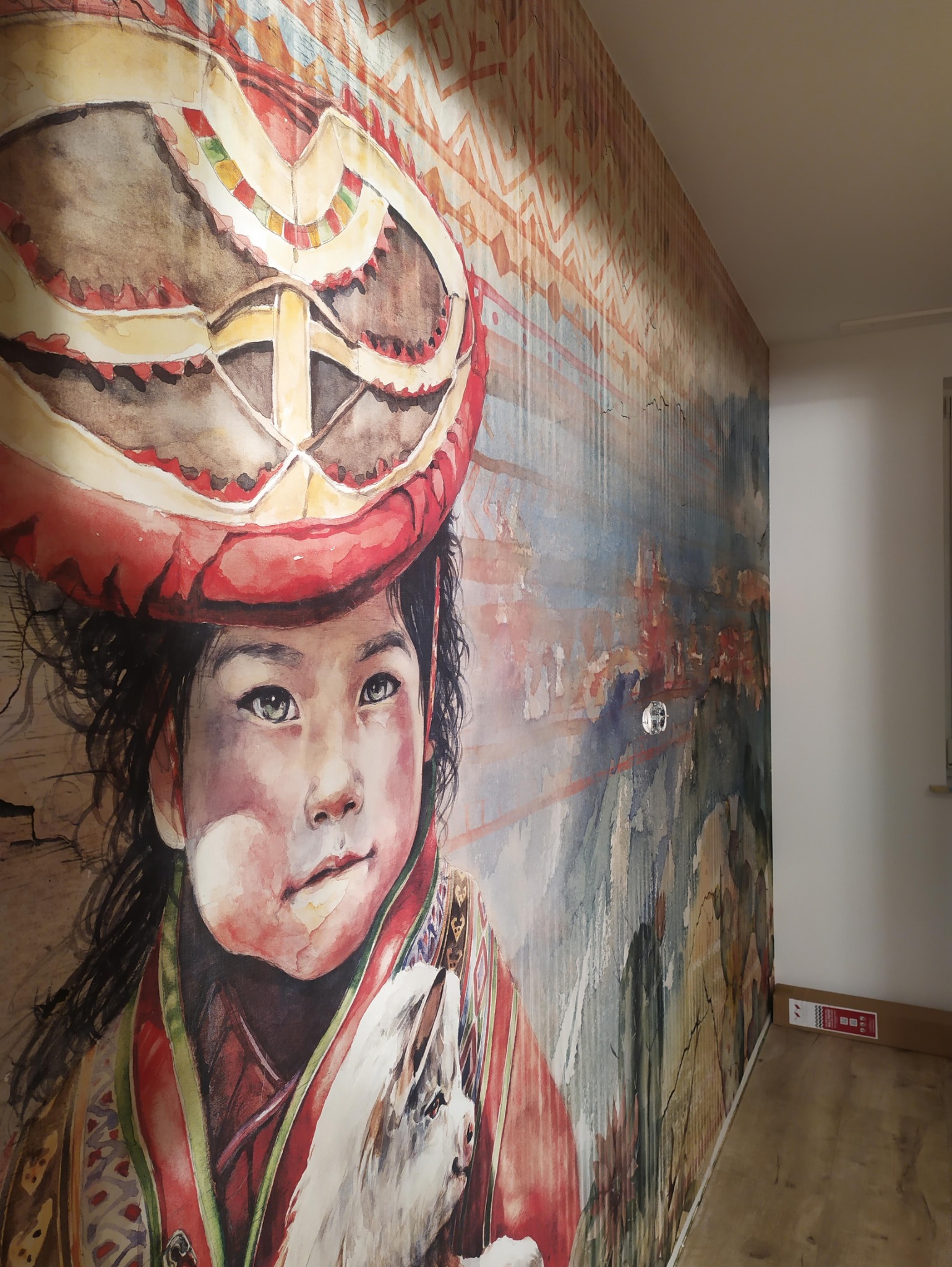 Wnętrze z fototapetą przedstawiającą portret dziecka w tradycyjnym nakryciu głowy, z widoczną fakturą ściany i subtelnym oświetleniem.