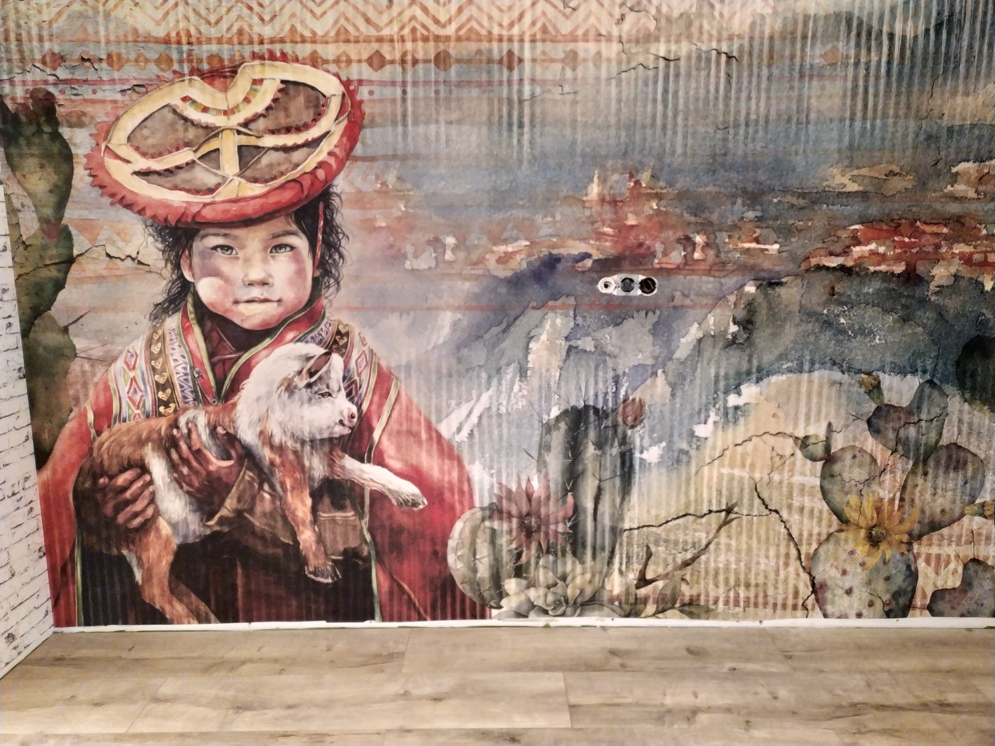 Fototapeta na ścianie z motywem dziewczynki w tradycyjnym stroju andyjskim trzymającej lamę, w tle góry i kaktusy, imitacja akwareli na teksturowanej powierzchni.