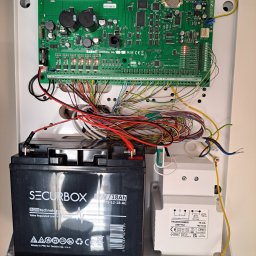 Federtech - Panel alarmowy Satel Integra 64 Plus z podłączonym akumulatorem Securbox 12V/18Ah i transformatorem Pulsar AWT752, widoczne kable i elektronika.