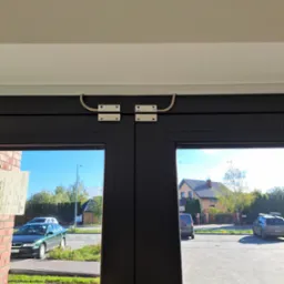 Czujnik magnetyczny na czarnych drzwiach wejściowych. Widok na ulicę z domami i samochodami. Element systemu alarmowego zamontowany na futrynie.