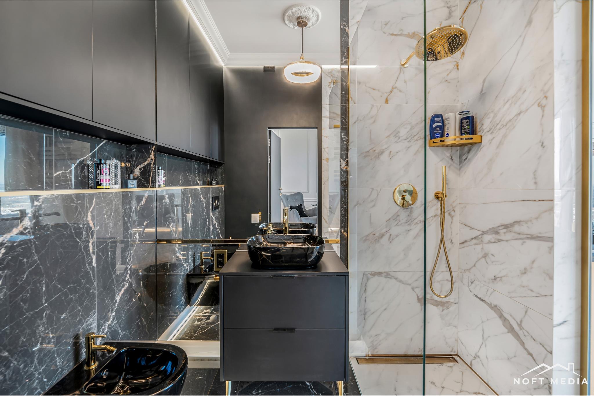Luksusowa łazienka z czarnymi marmurowymi ścianami, złotymi akcentami i kabiną prysznicową z białego marmuru, widok na pokój przez otwarte drzwi.