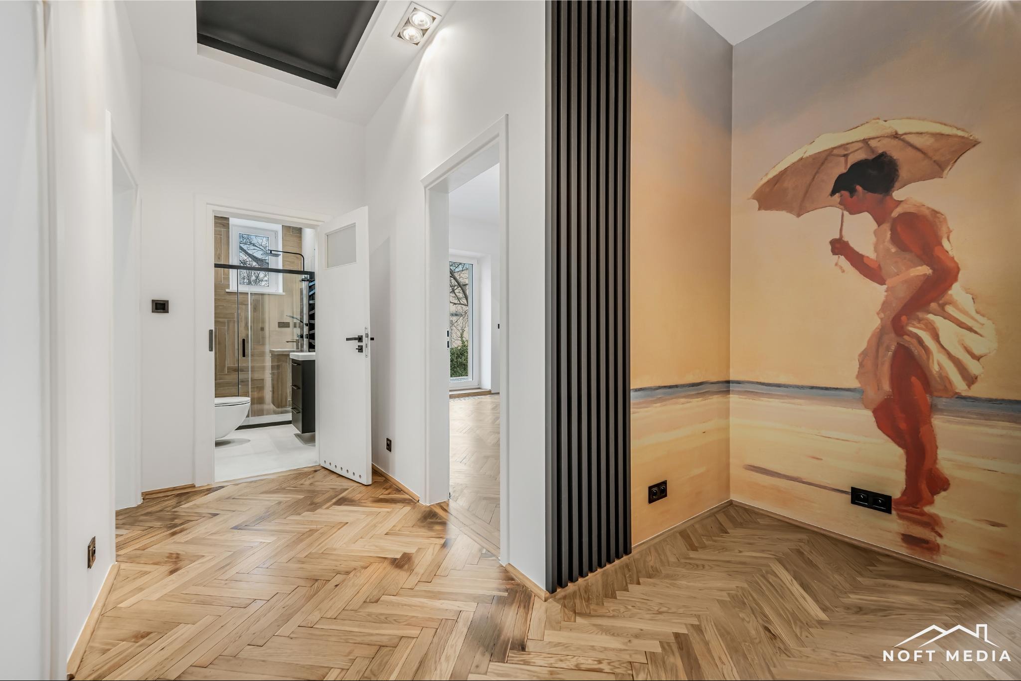 Korytarz z parkietem w jodełkę, białe ściany, otwarte drzwi do łazienki i pokoju, pionowe panele dekoracyjne oraz mural z kobietą z parasolem.