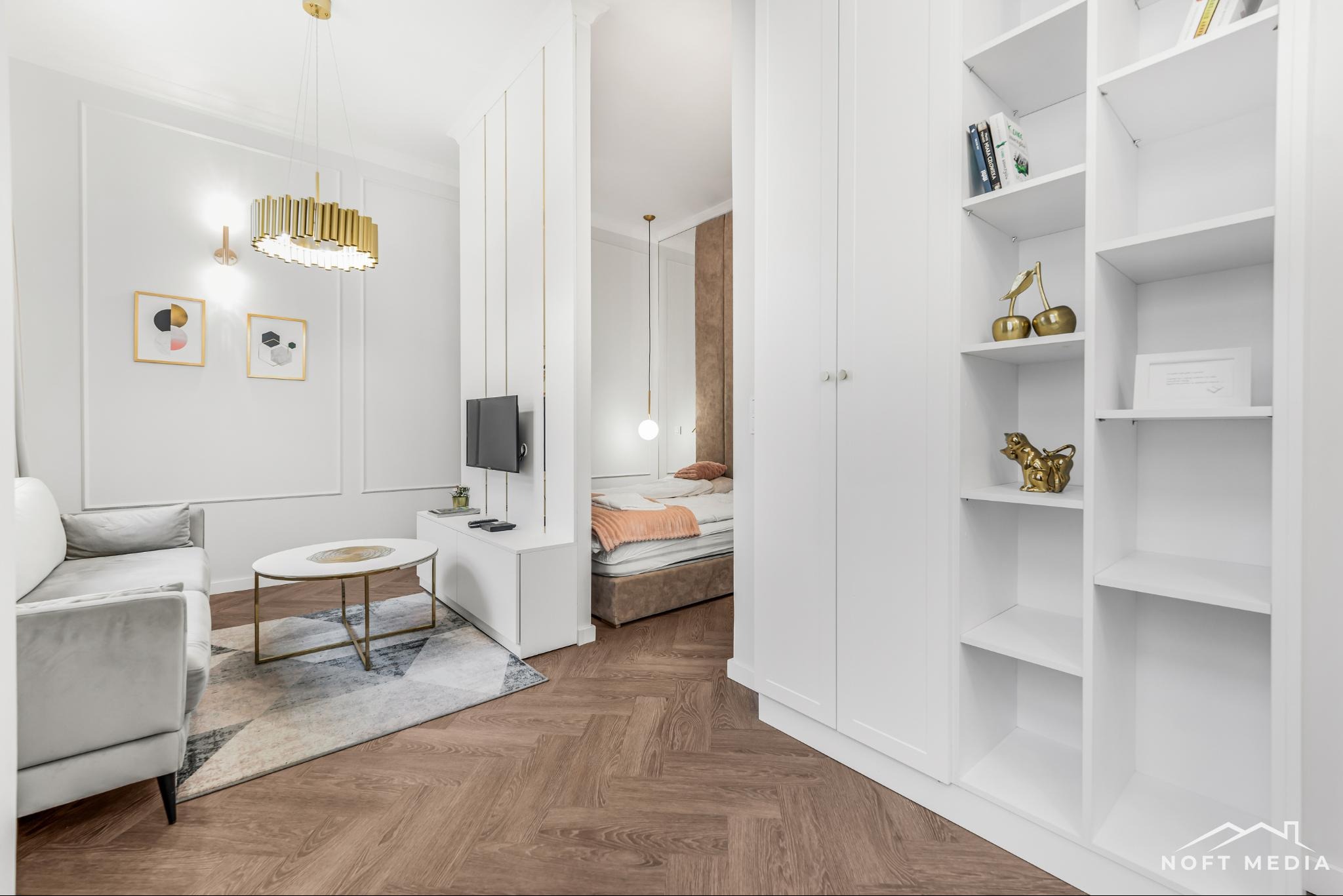 Nowoczesne wnętrze mieszkania w Piasecznie: salon z sofą i stolikiem kawowym przechodzi w sypialnię z łóżkiem, całość utrzymana w bieli i beżach z parkietem w jodełkę.