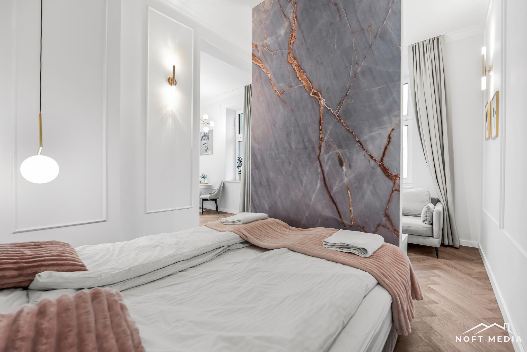 Nowoczesna sypialnia z łóżkiem typu king-size, marmurową ścianą działową z żyłami w kolorze miedzi, parkietem w jodełkę i minimalistycznym oświetleniem w kolorze złota.