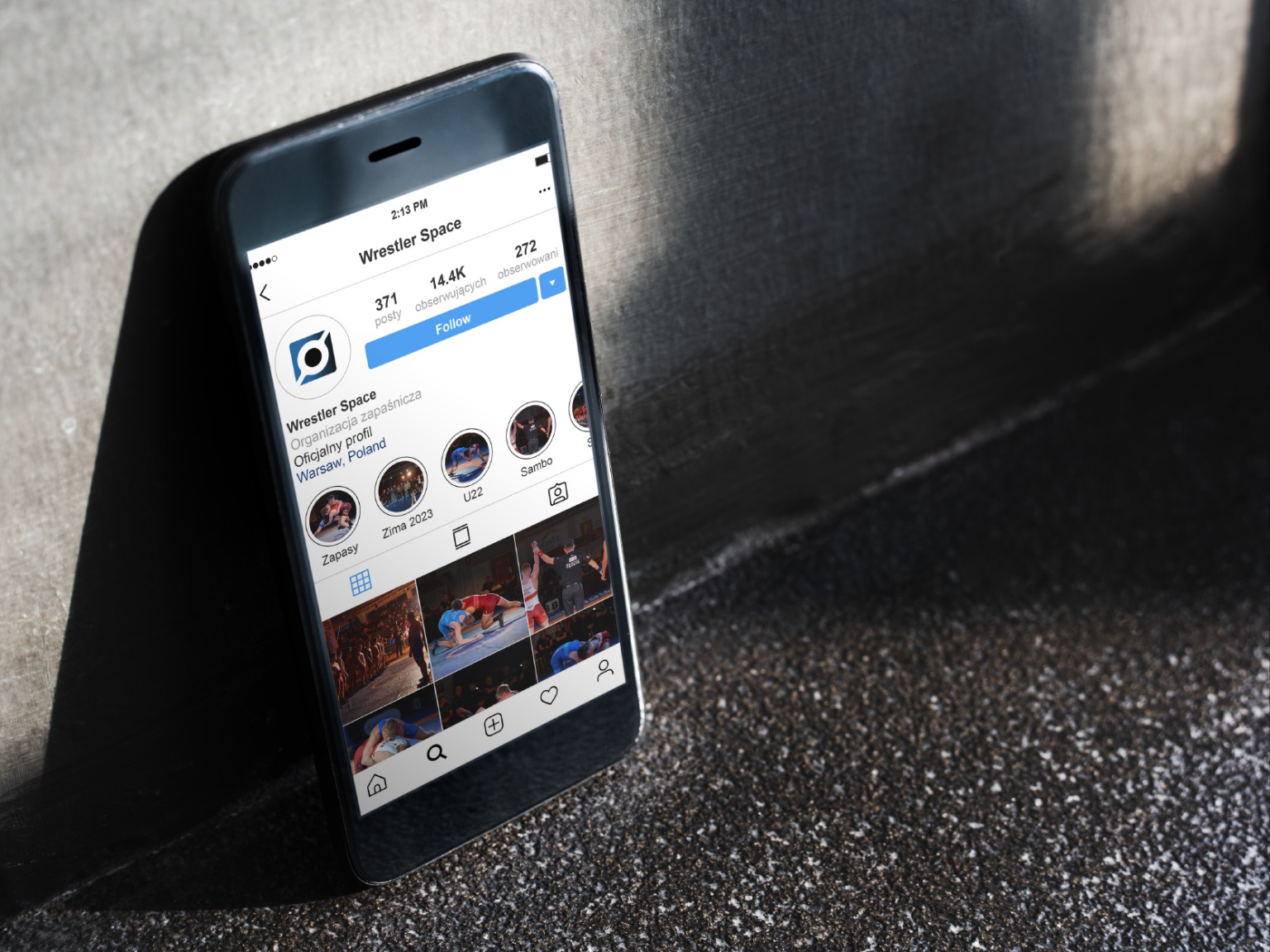 Smartfon wyświetla profil zapaśniczy 'Wrestler Space' z Warszawy na Instagramie, widoczne posty, obserwujący i informacje o organizacji.