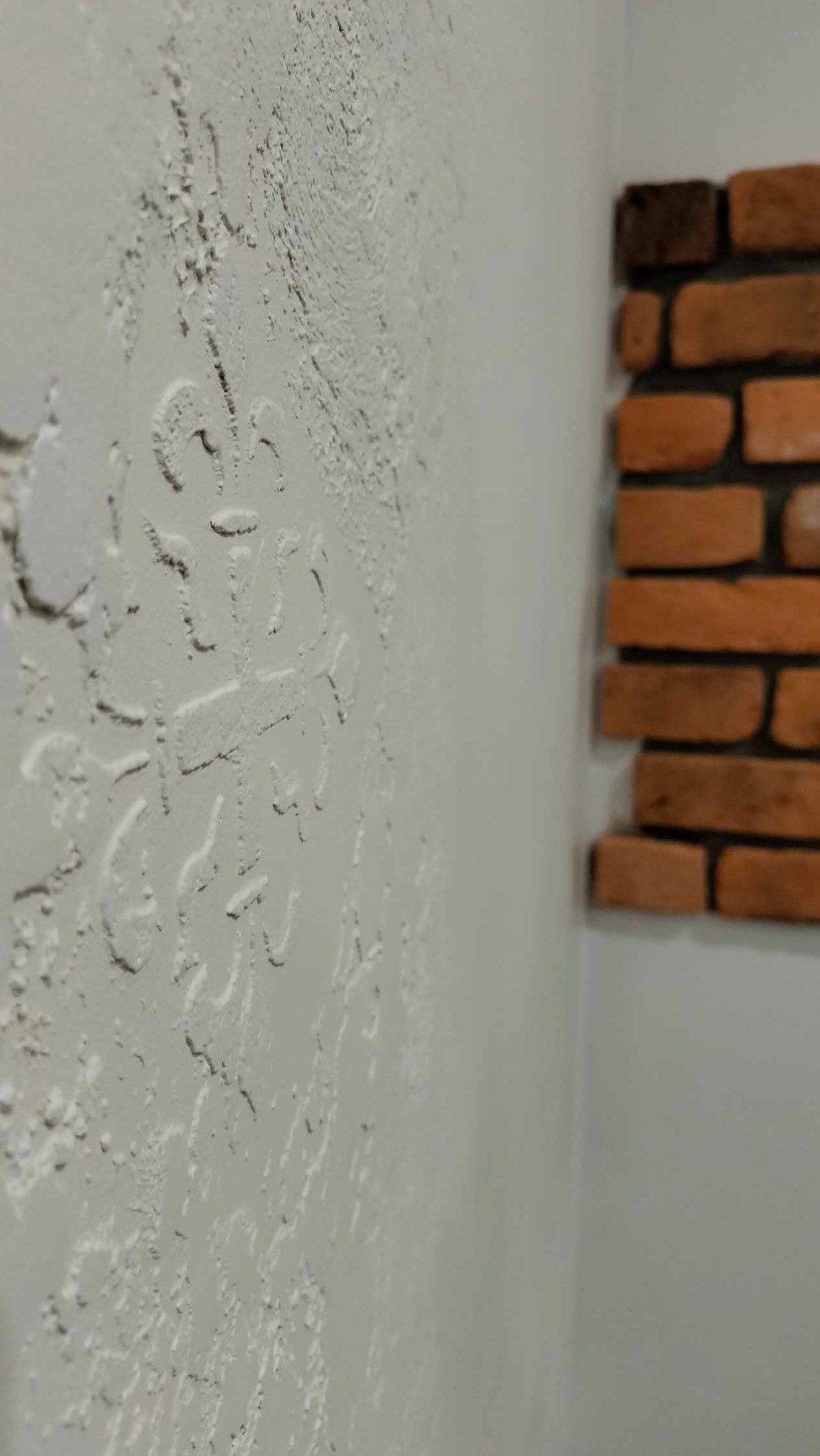 Dekoracyjna ściana z efektem struktury z subtelnym wzorem i fragmentem ściany z cegły w tle.