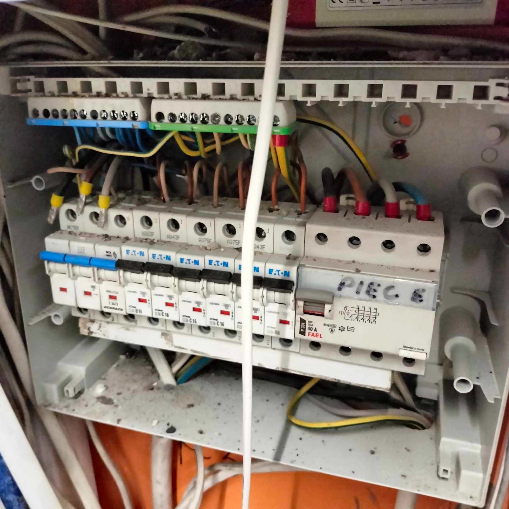 Rozdzielnica elektryczna z bezpiecznikami Eaton i przewodami w różnych kolorach, widoczne oznaczenia 'PIEC E' na jednym z wyłączników.