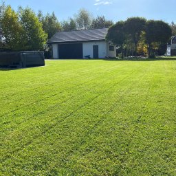 SoilCraft - Równomiernie skoszony trawnik przed domem z garażem i jacuzzi, widoczne ślady po kosiarce, słoneczny dzień.