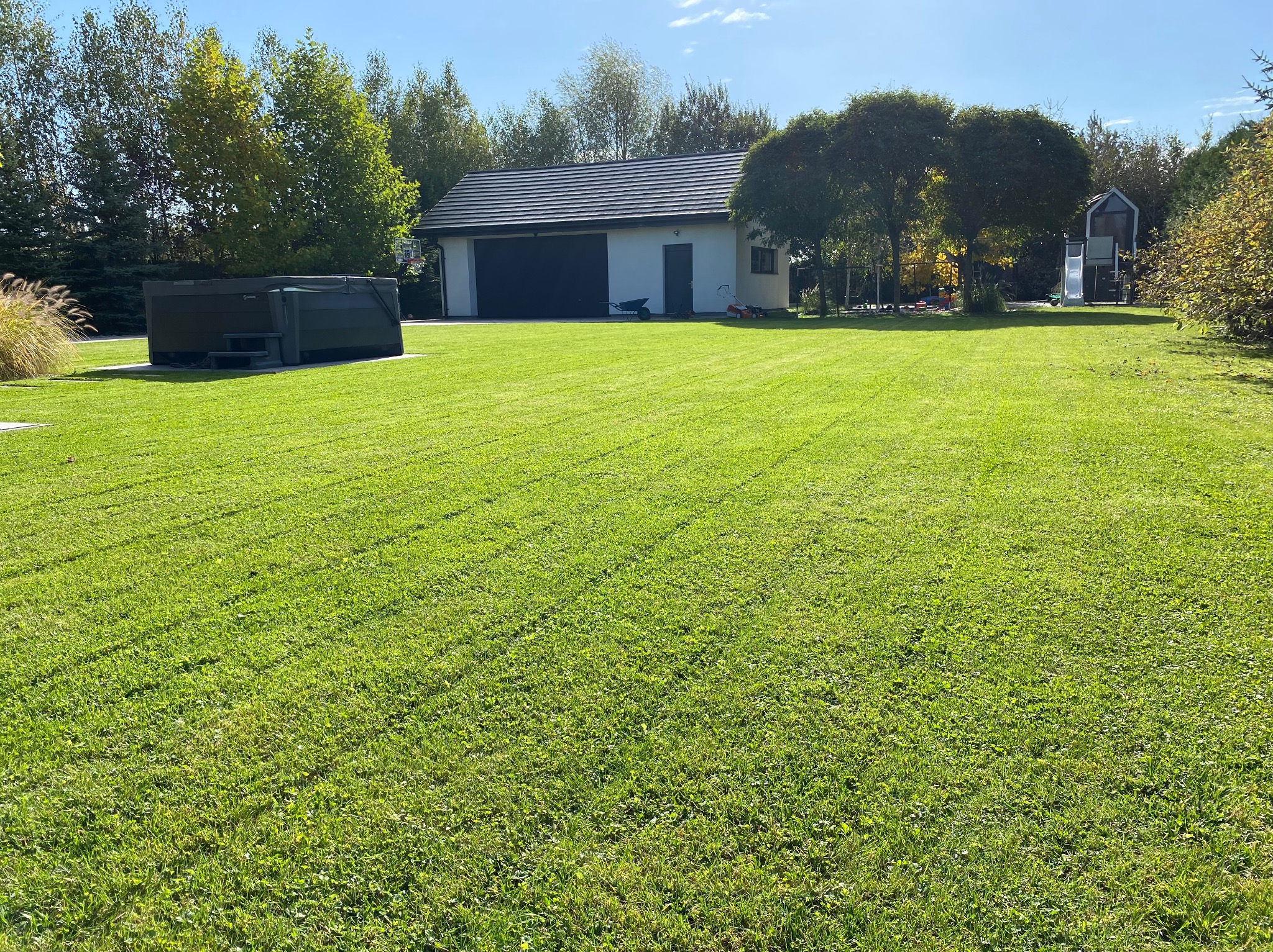 Równomiernie skoszony trawnik przed domem z garażem i jacuzzi, widoczne ślady po kosiarce, słoneczny dzień.
