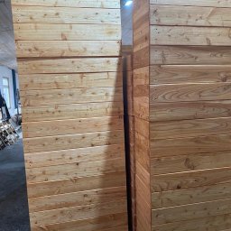 PAS-DOM SPÓŁKA Z OGRANICZONĄ ODPOWIEDZIALNOŚCIĄ - Panele z jasnego drewna ułożone w stos, widoczne sęki i usłojenie, zarys palet w tle.