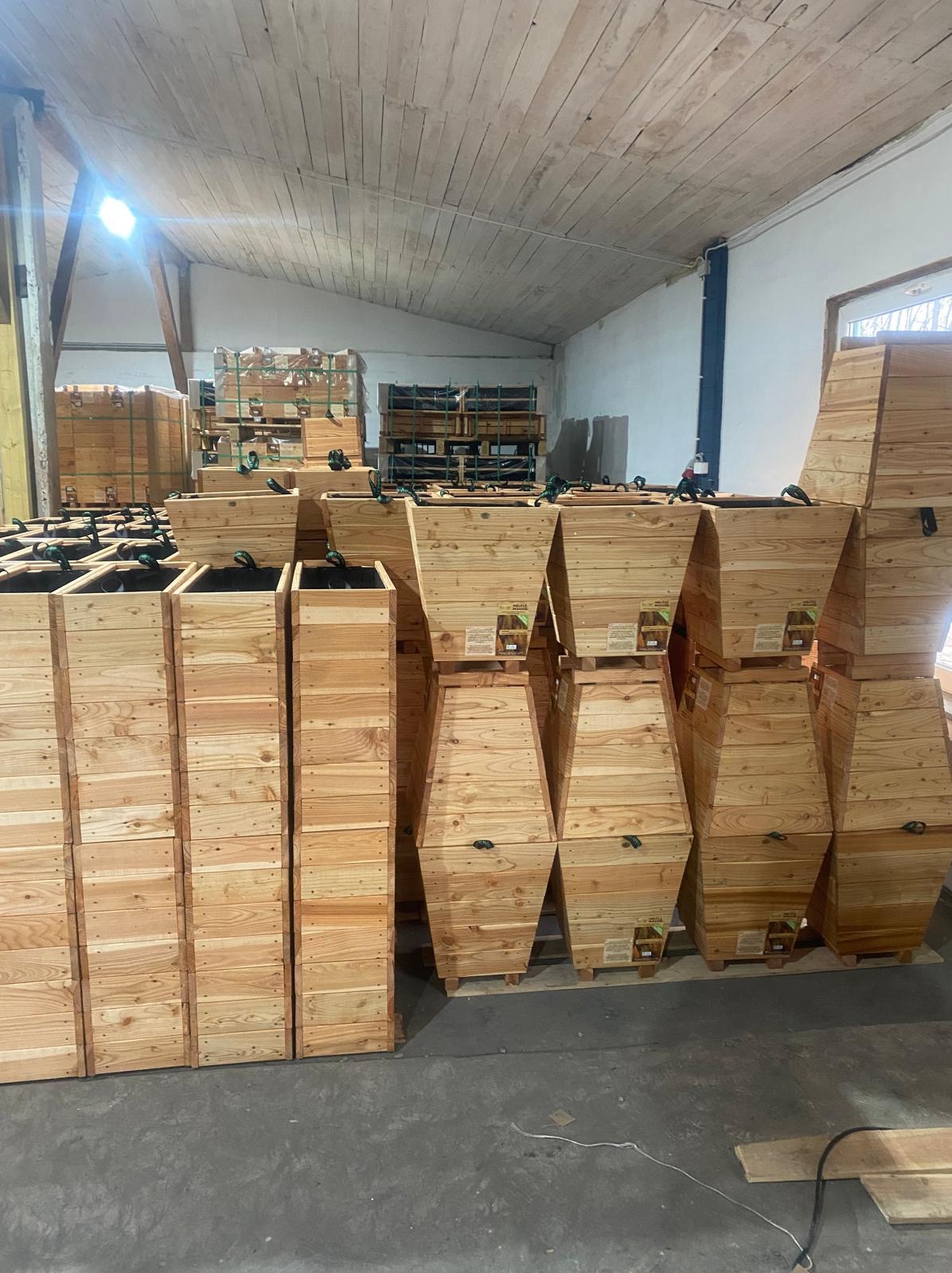 Magazyn wypełniony nowymi, drewnianymi skrzyniami na rośliny, ustawionymi w rzędach i na paletach, gotowymi do transportu.