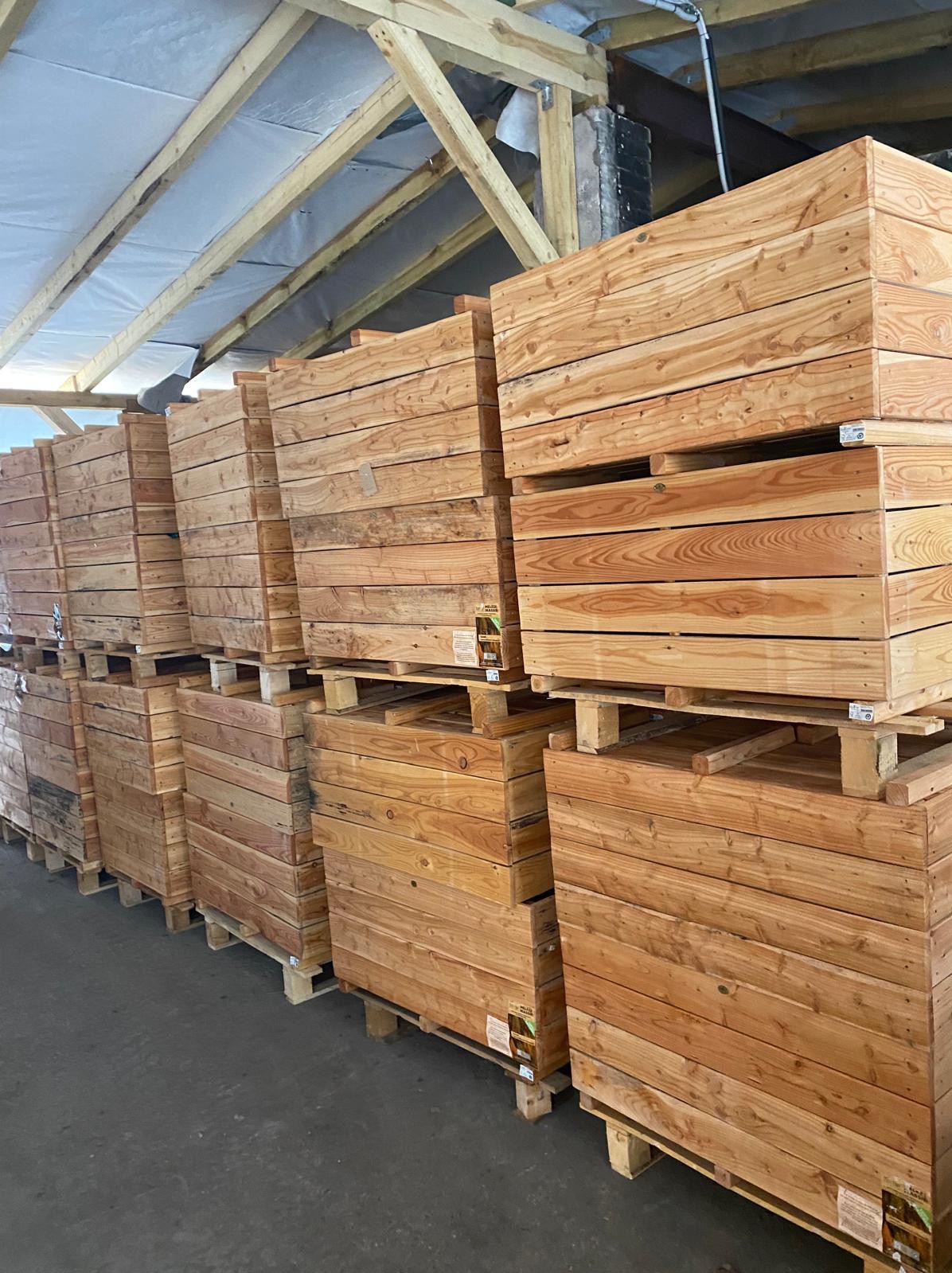Magazyn wypełniony paletami z drewnianymi skrzyniami, widoczne elementy konstrukcji dachu