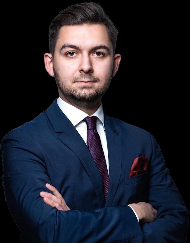 Portret młodego mężczyzny w granatowym garniturze, białej koszuli i bordowym krawacie, z rękami skrzyżowanymi na piersiach, na czarnym tle.