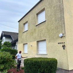 Firma Ogólnobudowlana Wiktor Marczak - Czyszczenie elewacji domu o beżowej strukturze, widoczny fragment wyczyszczonej ściany, pracownik z lancą ciśnieniową i adres 'Mińska 48'.