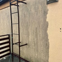 Firma Ogólnobudowlana Wiktor Marczak - Fragment elewacji z drabiną, ukazujący różnicę w czystości przed i po myciu. Widoczne zabrudzenia na części ściany, kontrastujące z czystą, jasną powierzchnią.