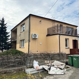 Firma Ogólnobudowlana Wiktor Marczak - Dwupiętrowy dom z beżową elewacją, balkonem i klimatyzacją. Widoczne ślady prac remontowych, rusztowanie i śmieci przy ogrodzeniu. Pochmurne niebo w tle.