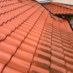 Firma Ogólnobudowlana Wiktor Marczak - Częściowo umyty, mokry dach z czerwonej dachówki karpiówki. Widoczny kontrast czystej i zabrudzonej powierzchni. Ujęcie z góry, lekki skos.