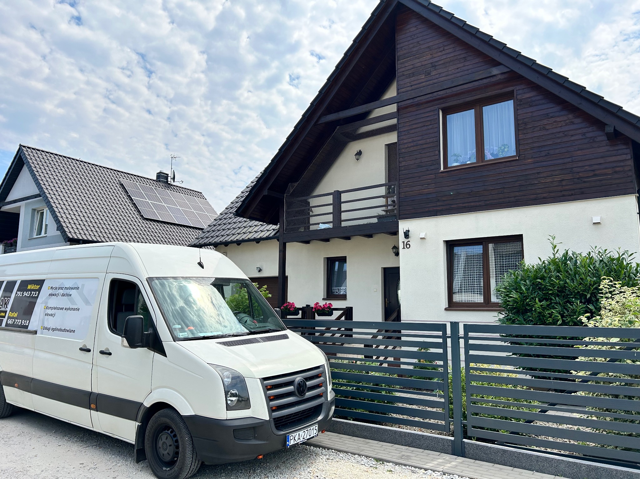 Dwukondygnacyjny dom z drewnianą elewacją i białymi ścianami, widziany zza szarego ogrodzenia. Na pierwszym planie biały bus z reklamą firmy elewacyjnej.