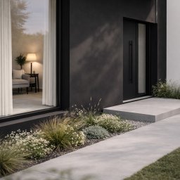 Pracownia Projektowa Klaudia Szkaradek - Nowoczesny dom jednorodzinny w Piwnicznej-Zdroju. Elewacja w odcieniach szarości i czerni, duże okno z widokiem na wnętrze, minimalistyczny ogród.