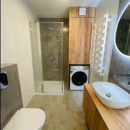 PerfectHouse Wykończenia Wnętrz Kamil Pazdan - Nowoczesna łazienka z kabiną prysznicową, umywalką nablatową na drewnianej szafce, pralką w zabudowie i grzejnikiem drabinkowym.