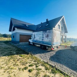 PerfectHouse Wykończenia Wnętrz Kamil Pazdan - Nowoczesny dom jednorodzinny z szarą elewacją i ciemnym dachem, przed którym stoi biała furgonetka z reklamą firmy specjalizującej się w ocieplaniu poddaszy metodą wdmuchiwania celulozy, widoczny...