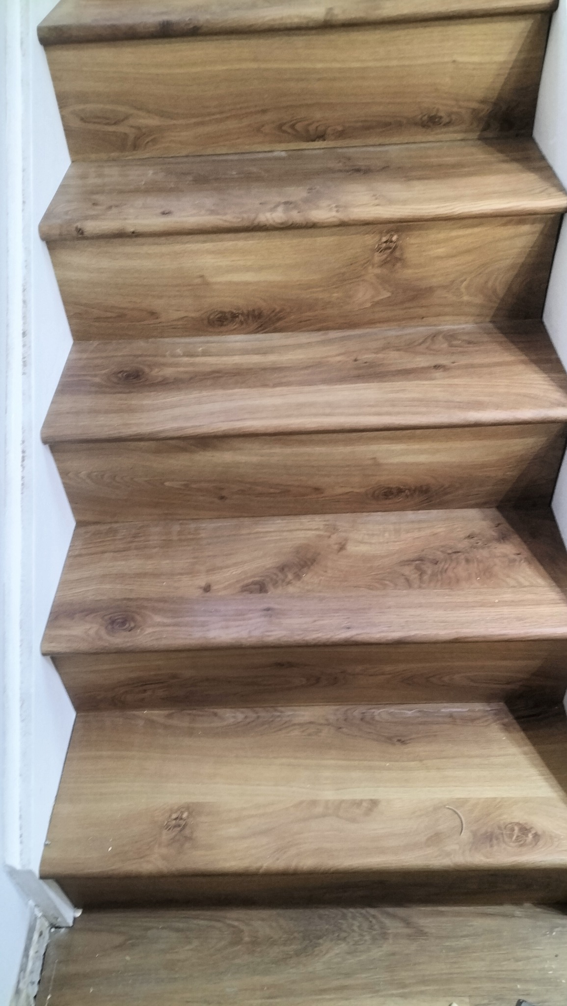 Wykończone schody z drewnopodobnymi panelami, widok z góry. Jasne, naturalne odcienie drewna, białe ściany po bokach. Detal wykończenia wnętrza.