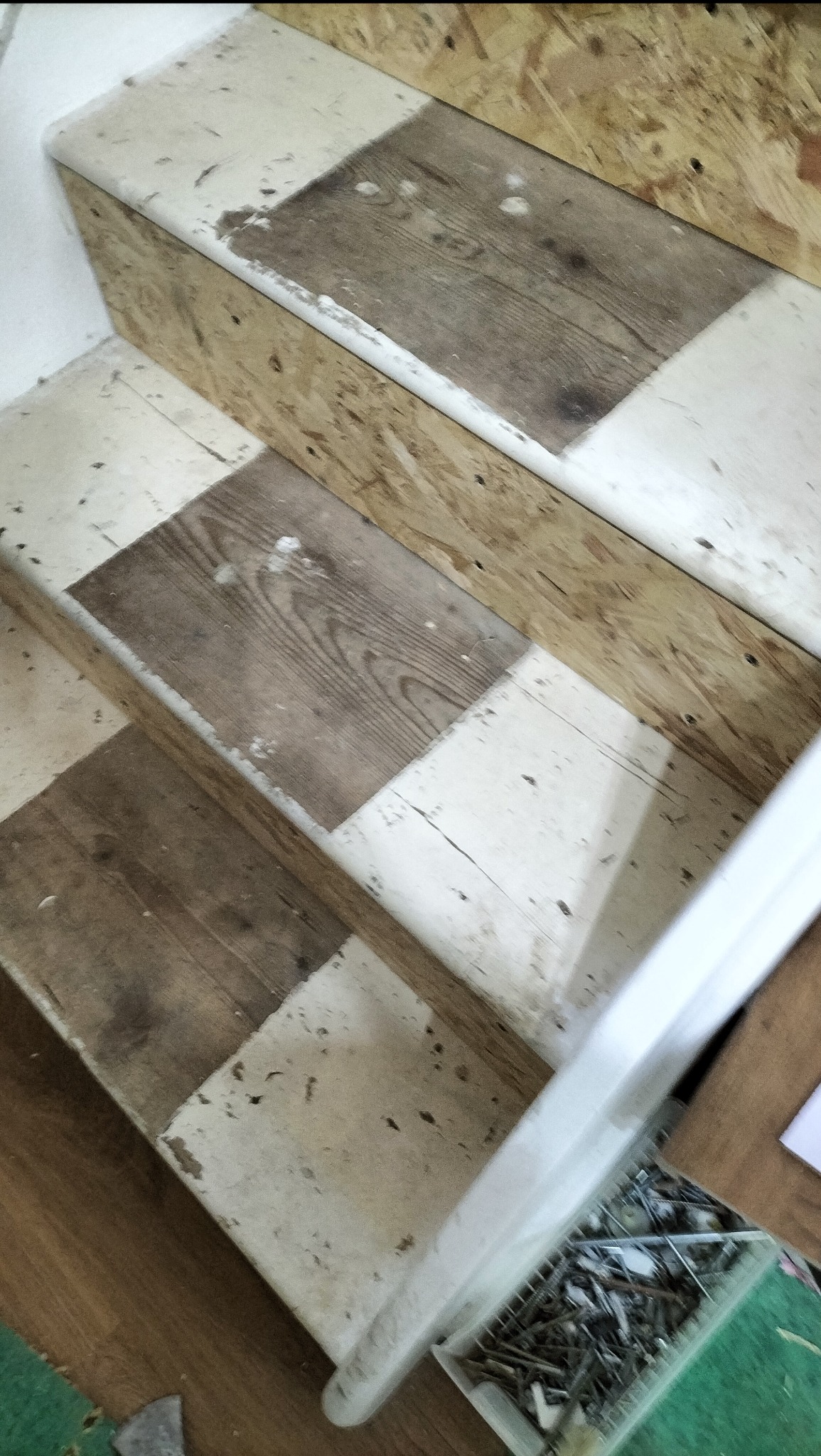 Schody w trakcie renowacji: widoczne drewniane stopnie z fragmentami starej farby i surowego drewna, przygotowywane do dalszych prac wykończeniowych. W tle narzędzia.