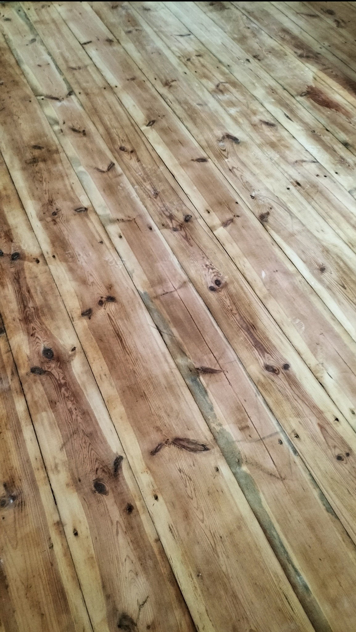 Ukończona podłoga z desek o ciepłym, brązowym odcieniu, ułożona pod kątem. Widoczne sęki i naturalny rysunek drewna. Podłoga po renowacji lub nowa.