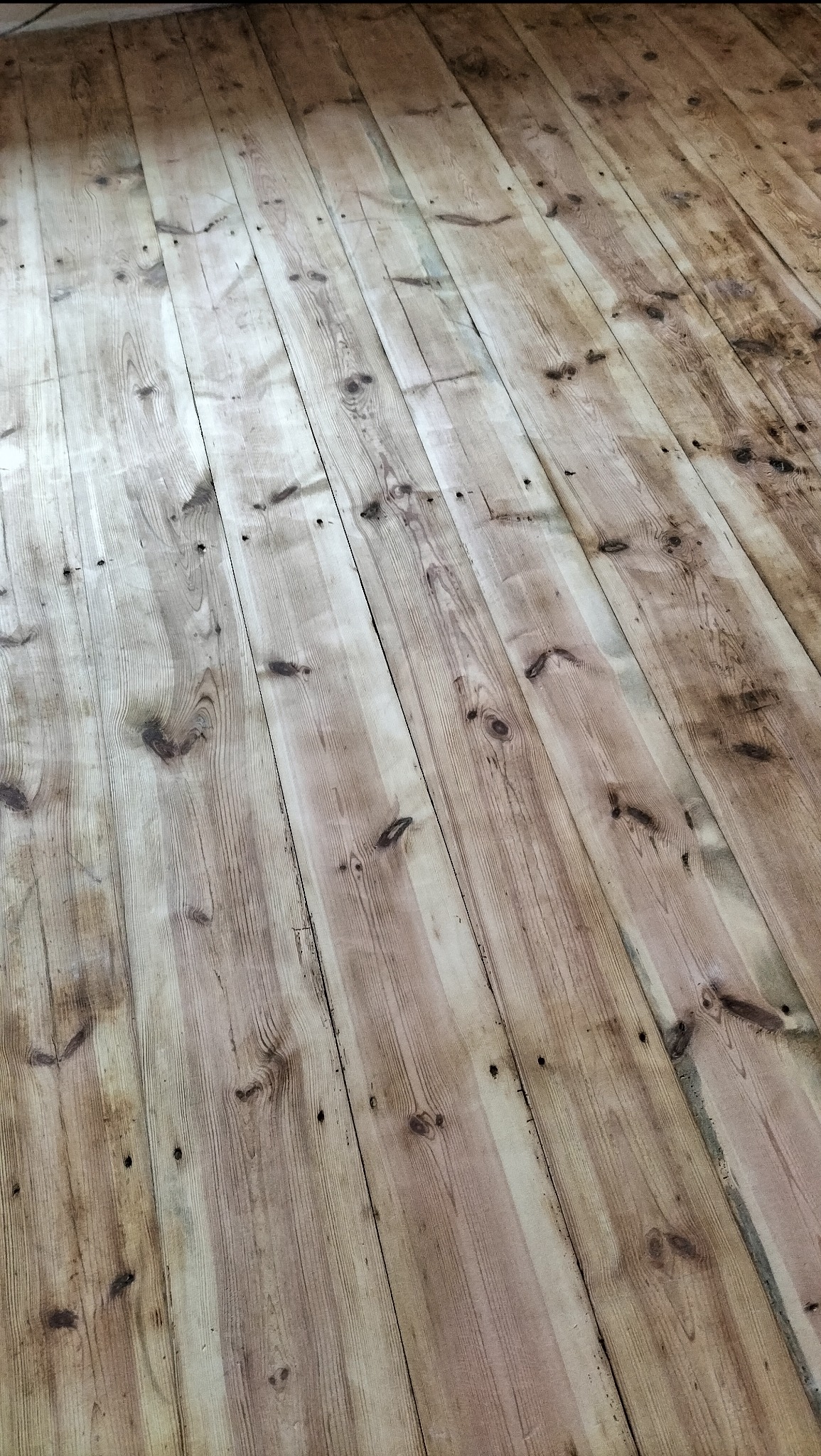 Deski podłogowe z widocznymi słojami drewna, ułożone równolegle, z delikatnymi przebarwieniami i śladami po gwoździach, tworzące rustykalny wzór podłogi.