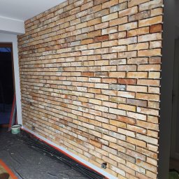 MXG Usługi Remontowe Marek Głomski - Ściana wyłożona dekoracyjną cegłą w odcieniach beżu i brązu, widoczna z bliska, z elementami przygotowania do dalszych prac wykończeniowych.