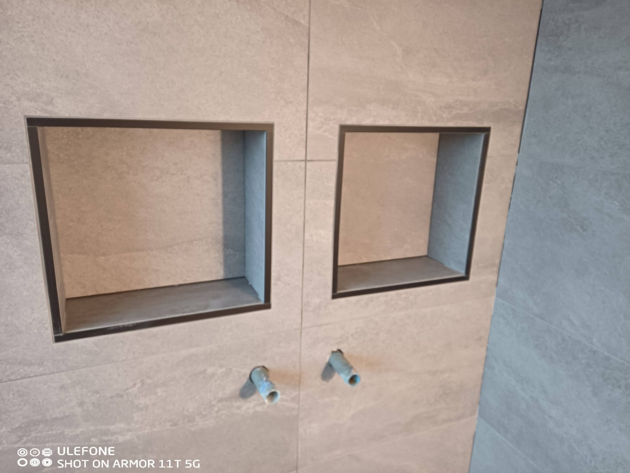 Wykończona ściana z dwoma wnękami w szarej płytce, widoczne rury, Dąbrowa Chełmińska. Minimalistyczny design, precyzyjne wykonanie, nowoczesna łazienka.