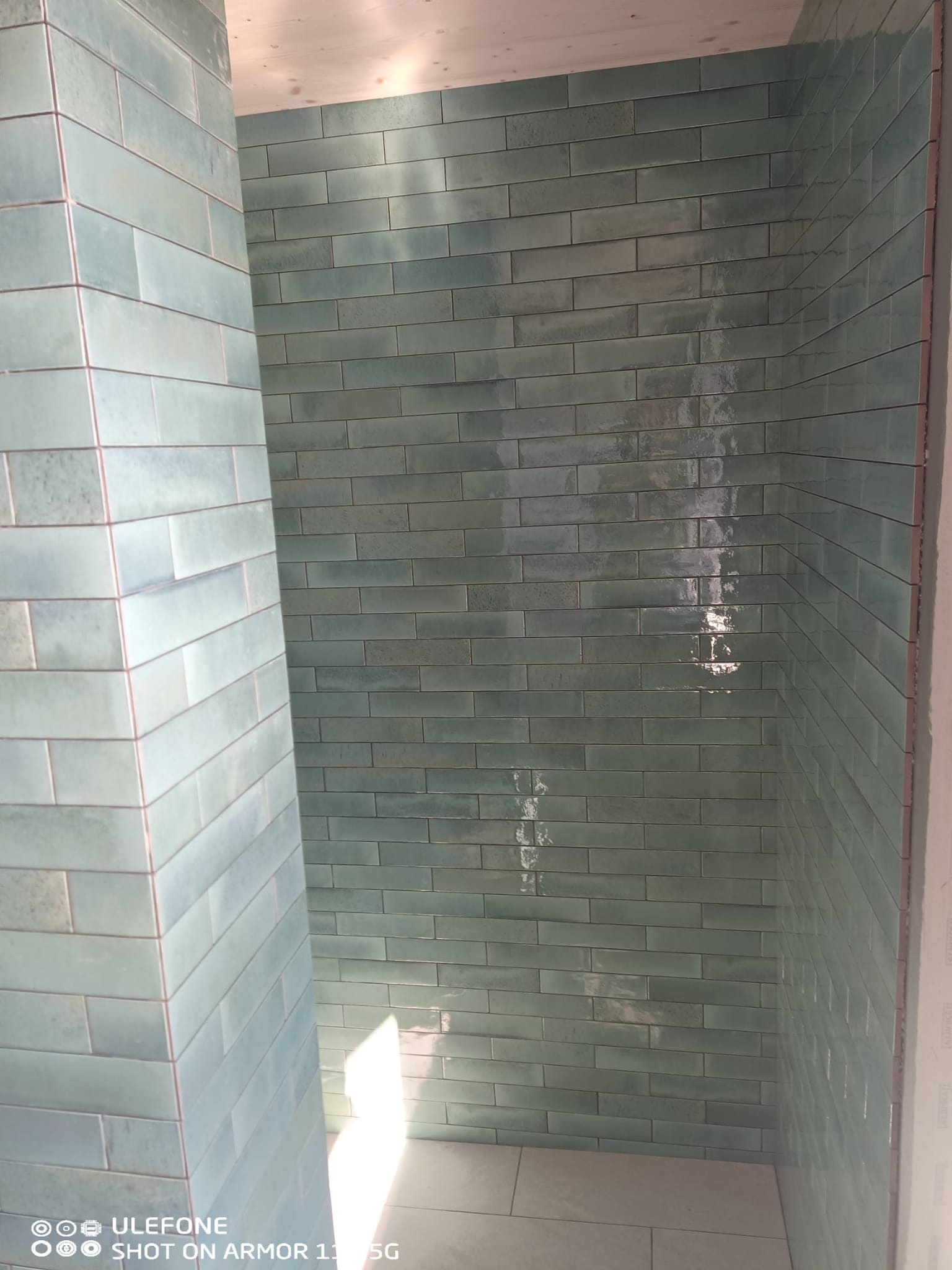 Świeżo położone, błyszczące, turkusowe płytki w kształcie cegiełek na ścianach i podłodze kabiny prysznicowej. Widoczny fragment narożnika.