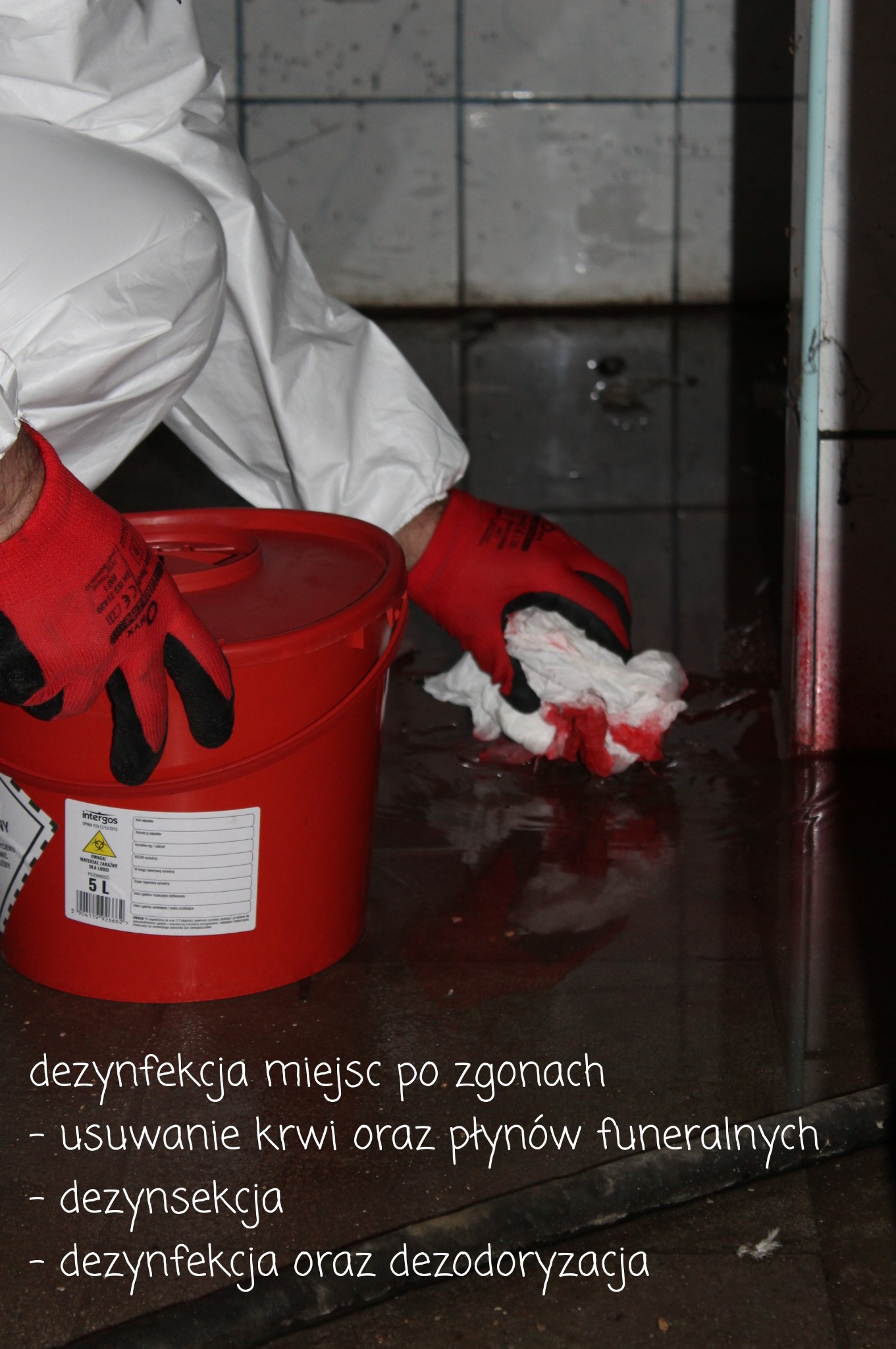 Pracownik w kombinezonie ochronnym i czerwonych rękawicach usuwa zabrudzenia z podłogi szmatką, obok stoi czerwone wiadro z etykietą ostrzegawczą o materiale zakaźnym.