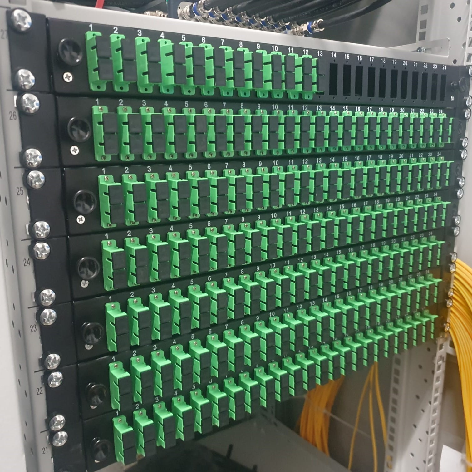 Panel krosowniczy światłowodowy z zielonymi adapterami SC, uporządkowane okablowanie w szafie rack, widoczne numery portów.